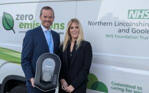 a man and woman stood in front of an electric car with a charger