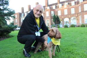 Man crouched down on grass holding a dog in front of him